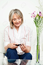 Smiling senior woman sitting on couch with smartphone