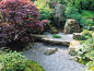 The careful landscaping in a Japanese garden invites one to stop and reflect. A large flat stone serves as a bench above a gravel groundcover.: 