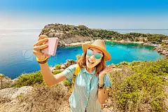 Asian Girl in a hat takes a selfie on the background of stunning views of the azure Bay in the Mediterranean sea. Travel, vacation and mobile connection conceptAsian Girl in a hat takes a selfie on the background of stunning views of the azure Bay in the 