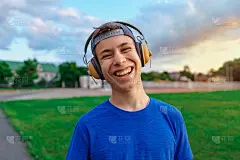 快乐少年肖像在一个体育场，他戴着耳机和微笑，一个足球场绿色的草地-运动和健康的概念