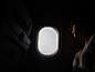 A dim shot of a person sitting next to an oval airplane window