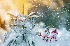两个有趣的小玩具娃娃雪人在编织的帽子和围巾在深雪户外附近的松树树枝。新年快乐，并附上圣诞贺卡。