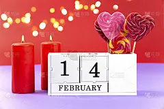 2月14日紫色时尚背景与散景。2 .燃烧的红烛，一个万年历块与2月14日的日期和甜蜜的爱情焦糖心