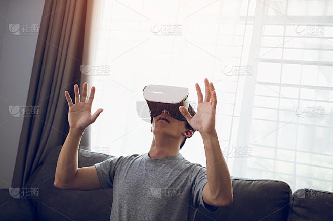 年轻的亚洲男子戴着虚拟现实眼镜在客厅欣赏...