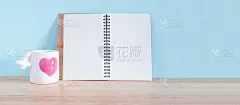 木桌和浅蓝色的墙壁上摆放着白色陶瓷咖啡杯，粉红色的心和打开的书。献给你情人节的背景。