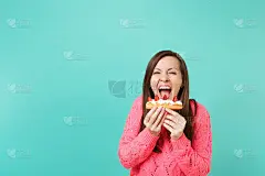 愉快的年轻女子针织粉红色毛衣保持嘴大开，在手，咬饼孤立在蓝色墙壁背景，工作室肖像。人们生活方式的概念