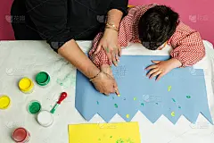 特殊教育的老师和学生穿着长袍，在桌子上用手画着生日花环和涂着丙烯颜料的黄色纸板。塑料工艺疗法。