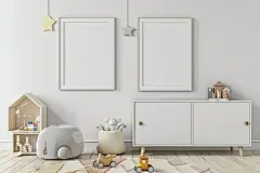 点击来源直接获取大图文件 |两个空白相框悬挂在极简主义托儿所的白色橱柜上方，非常适合展示艺术品或家庭照片。房间里有一个毛绒灰色玩具、一个木制玩具火车、一个米色储物篮