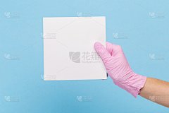 一只戴着粉色医用手套的女性手拿着一张蓝色背景的空白纸。模拟，名片