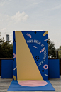 This may contain: a large blue and yellow sculpture sitting on top of a wooden floor next to trees