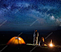 浪漫对游客在他晚上篝火和对星空的帐篷附近的营地