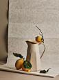 This may contain: two lemons are sitting on a plate next to a white pitcher with green leaves