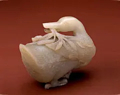 青玉回首鸭 
        青玉回首鸭，清，长15cm，宽6cm，高10.5cm。 
        玉呈青白色，微透光，质地温润清朗。鸭身肥硕，圆臀阔胸，短颈，短翅，翅及鸭身有排列整齐的羽，并布满仿古勾云纹。鸭作回首状，一足踏于地，一足向前，似在行走中。其口衔谷梗，梗垂于鸭身，谷叶似飘似摇。 此作品造型生动准确，栩栩如生。六畜、家禽为玉雕动物中最常见的题材，自唐代之后，玉鸭之作多出新样。同历代作品相比，此件玉鸭更为精致，其背负的谷穗既有岁岁平安之意又有五谷丰登之祈，寓意不俗，是一件艺术水平很高的作@北