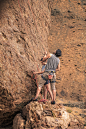 man in gray t-shirt and blue denim shorts climbing brown rock during daytime