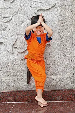 在泰国的中国寺庙里，穿着少林和尚橙色衣服的小女孩在做欢迎表达崇敬的动作。