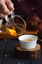 健康饮料的概念。将刚泡好的茶从玻璃罐中倒入置于深色背景的木板上的瓷杯中
