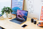 Open laptop displaying mountain on desk with framed posters, a plant, and lenses