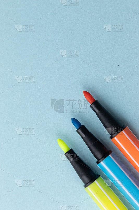 淡蓝色背景上的黄色、橙色和蓝色毡尖笔。平放顶视图与复制空间。