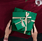 This may contain: two hands holding a green gift box with white ribbon