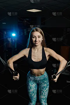 活泼漂亮的健身模特女孩在健身房的模拟器上训练胸肌