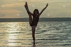 美丽苗条的女孩在泳衣做体操，瑜伽，跳舞的背景，日出，日落。少年和体育