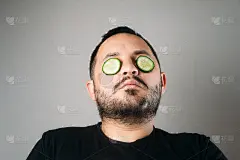 胡子松弛的年轻人脸上敷着黄瓜保湿面膜