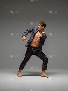 时尚的年轻人霹雳舞穿着衣服赤裸的躯干和赤脚跳舞在工作室孤立的灰色背景