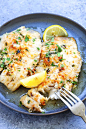 Parmesan tilapia on a plate and served with fork and lemon wedges.