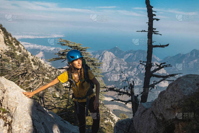 登山者站在山顶上。带着头盔和背包山的女登...