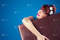 漂亮的海报女郎摆姿势与复古手提箱对抗蓝色