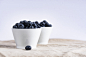 two white ceramic cup filled with blueberries fruit place on brown textile