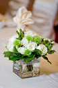 DIY rose centerpiece, you will need a cube vase, short white roses, green carnations and greenery.     Lots of other cheap DIY rose centerpieces at http://www.cheap-wedding-solutions.com/diy-wedding-centerpieces-roses.html: 