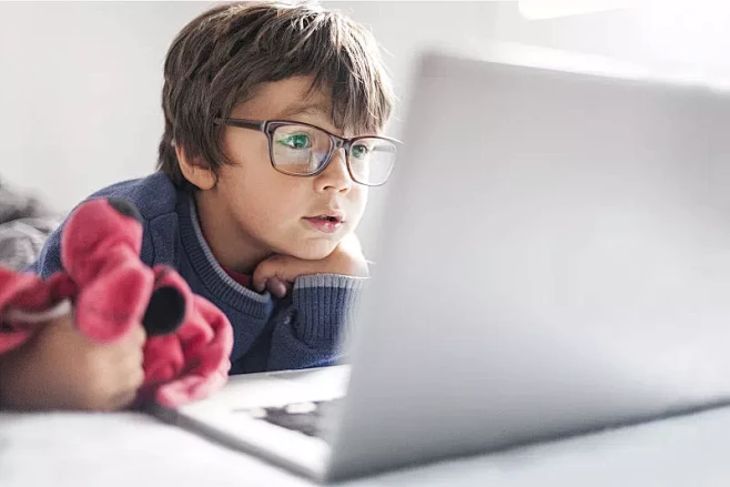 小男孩戴着超大眼镜看笔记本电脑的肖像图片...