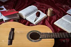 吉他躺在红色的织物上，干花，书在红色的背景下，散书，钢笔，艺术氛围