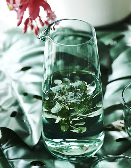 摆放在叶子上的绿色玻璃水瓶里盛放着水和香...