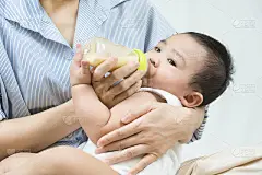 在床上，母亲用玻璃奶瓶喂婴儿。早上好。早餐时间。健康饮食。的童年。