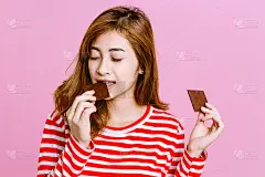 粉红背景下的美女在吃黑巧克力