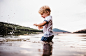 A wet, small toddler boy standing outdoors in a river in summer, playing.