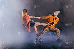 一对情侣在跳现代舞，展示他们的腿部伸展动作。黑色的背景，而这对夫妇穿着城市色彩鲜艳的衣服。