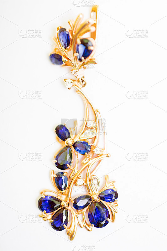 金色耳环与蓝色蓝宝石和立方锆石上的白色背...