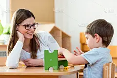 年轻的女人看着聪明的孩子玩的教育彩色玩具室内-幼儿园