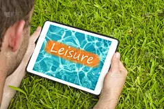 一个年轻人躺在花园里的草地上，用平板电脑看着水背景，上面写着“休闲”