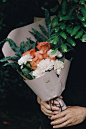 A person holding bouquet of white carnations and pink roses wrapped in decorative paper