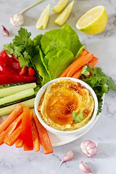 鹰嘴豆泥，不同的蔬菜，生菜叶，柠檬和大蒜在一个明亮的背景。素食食物。
