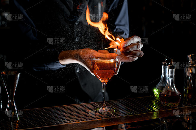 特写的鸡尾酒杯，调酒师洒柑橘汁，点燃。