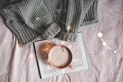 圣诞杯咖啡，打开的书和编织的面料在床上灯光下。冬季。-早上好顶部视图.