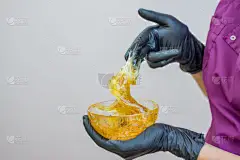 脱毛和美容概念-糖糊或蜡蜂蜜脱毛与黑手套美容师在温泉沙龙的手