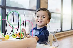 Happy little boy plays with toySmiling toddler boy plays with bead rollercoaster while waiting in a pediatrician's waiting room.