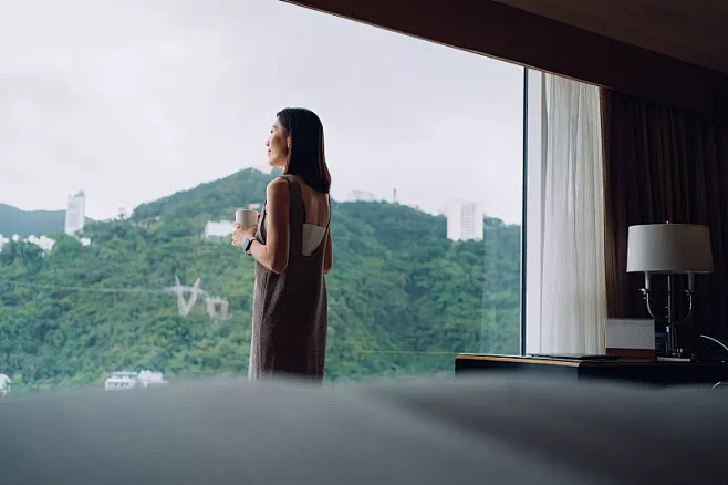 年轻的亚洲女人喝着咖啡，在舒适的家里靠窗...