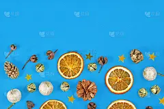 季节性的圣诞公寓陈设着干橙子片、冷杉球果、圣诞树装饰品和蓝色背景上的金铃
